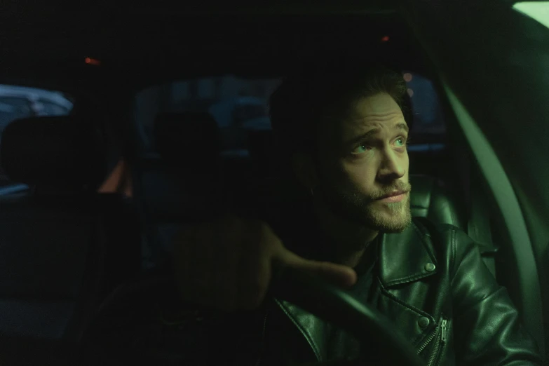 a man in a leather jacket sitting in a car, by Elsa Bleda, trending on pexels, photorealism, charlie cox, green lights, still from riverdale, pitch black room