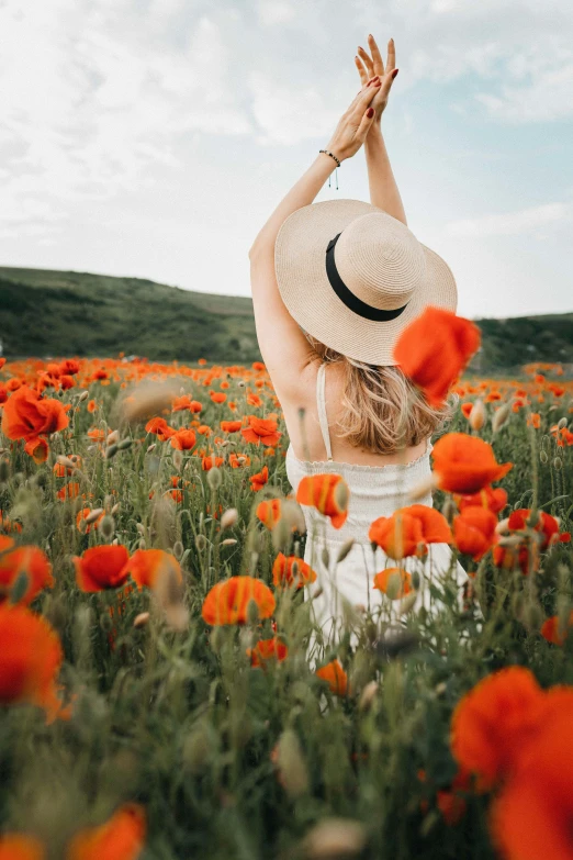 a woman sitting in a field of red flowers, unsplash contest winner, white and orange, red hat, with arms up, poppy