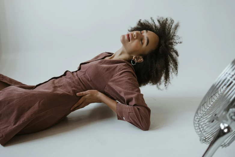 a woman laying on the floor in front of a fan, by Nina Hamnett, trending on pexels, brown jacket with long sleeves, ashteroth, studio shoot, wearing human air force jumpsuit