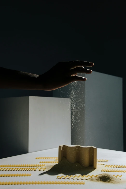 a close up of a person's hand near a box of pasta, an abstract sculpture, inspired by Lucio Fontana, trending on unsplash, conceptual art, light rays illuminate dust, ignant, levitating sand, tabletop model
