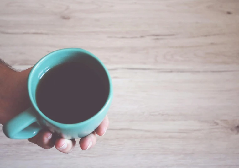 a person holding a cup of coffee on a wooden floor, pexels contest winner, minimalism, black and teal paper, drinking cough syrup, brilliantly coloured, secret tea society