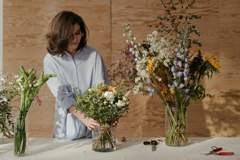 a woman arranging flowers in vases on a table, by Alice Mason, trending on unsplash, wrapped in flowers and wired, large tall, ignant, slightly minimal