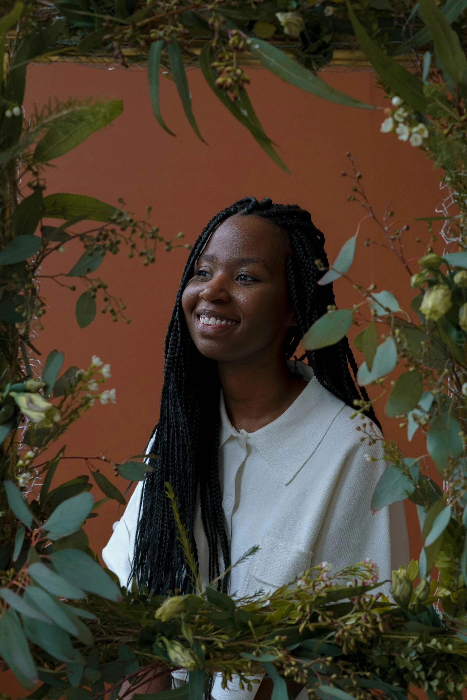 a woman standing in front of a wreath of flowers, by Dulah Marie Evans, archways made of lush greenery, emmanuel shiru, in front of an orange background, hammershøi