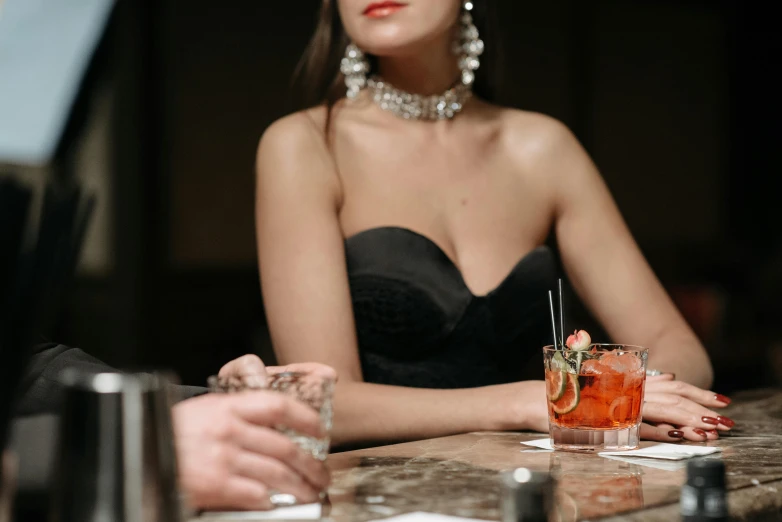 a woman in a black dress sitting at a bar, trending on pexels, cleavage, man and woman, background image, diamonds around her neck