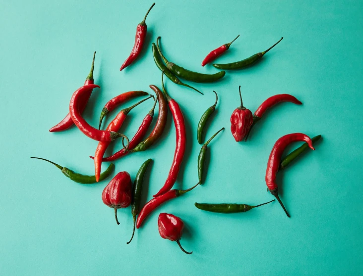 a group of chili peppers sitting on top of a blue surface, olive green and venetian red, dezeen, front facing shot, swirling around