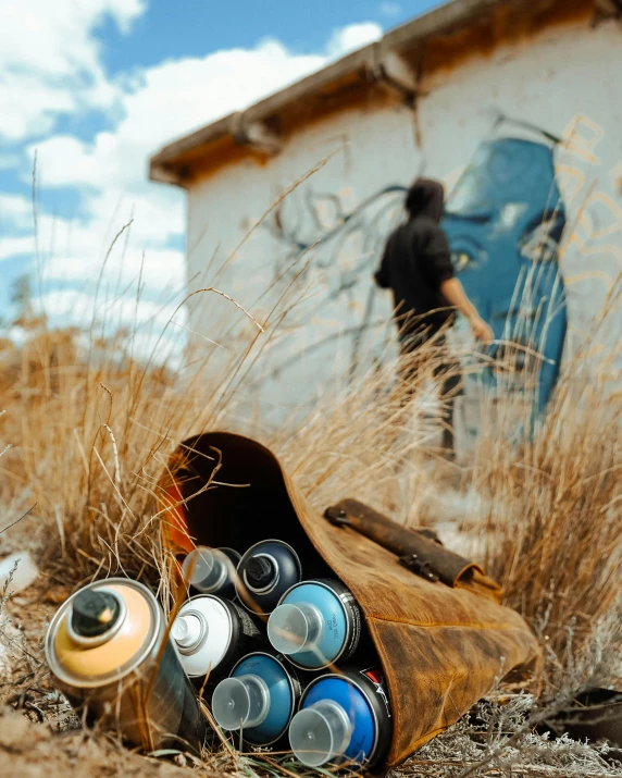 a bunch of cans that are sitting in the dirt, an airbrush painting, by Jesper Knudsen, pexels contest winner, graffiti, standing outside a house, in a dried out field, blue paint on top, photo of a man