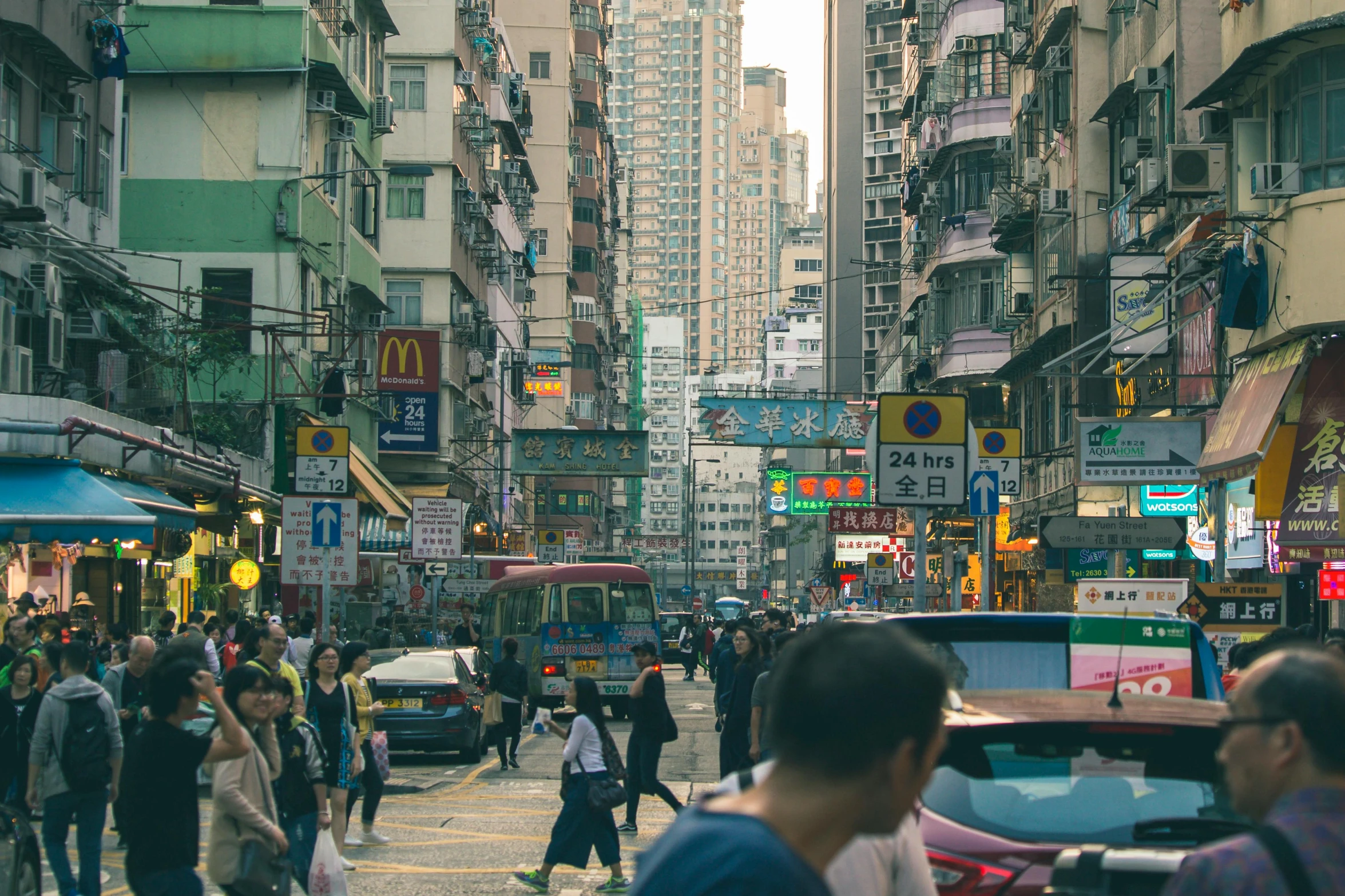 a group of people walking down a street next to tall buildings, city like hong kong, a bustling magical town, image