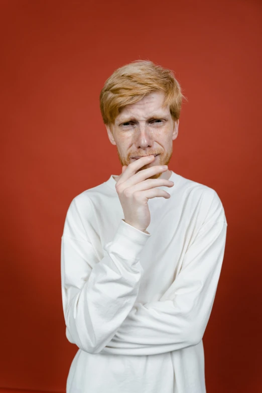 a man standing in front of a red wall, an album cover, by Lasar Segall, wearing white clothes, ginger hair with freckles, 15081959 21121991 01012000 4k, john carmack