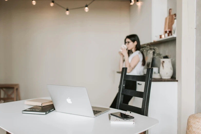 a laptop computer sitting on top of a white table, a picture, by Carey Morris, trending on pexels, female looking, table in front with a cup, sitting on a chair, looking from shoulder