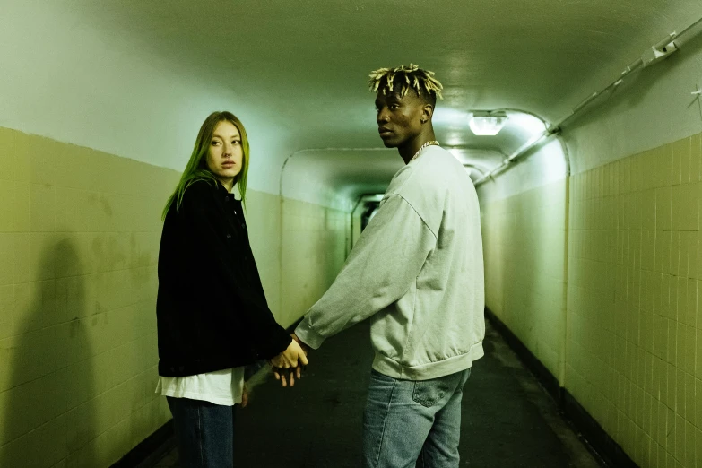 a man and a woman holding hands in a hallway, an album cover, inspired by Elsa Bleda, trending on pexels, antipodeans, black man, green clothing, bleached, live action movie