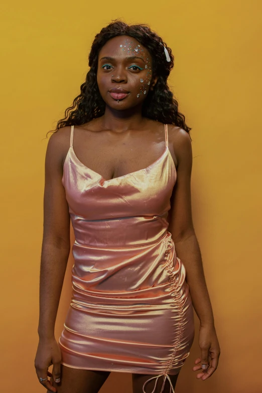 a woman standing in front of a yellow wall, an album cover, by Chinwe Chukwuogo-Roy, trending on pexels, renaissance, wearing a pink dress, metallic torso, studio portrait, wearing a camisole