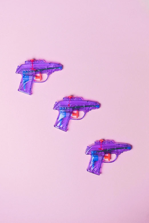 a close up of three toy guns on a pink surface, purple and blue neons, silicone patch design, on a pale background, 1 8