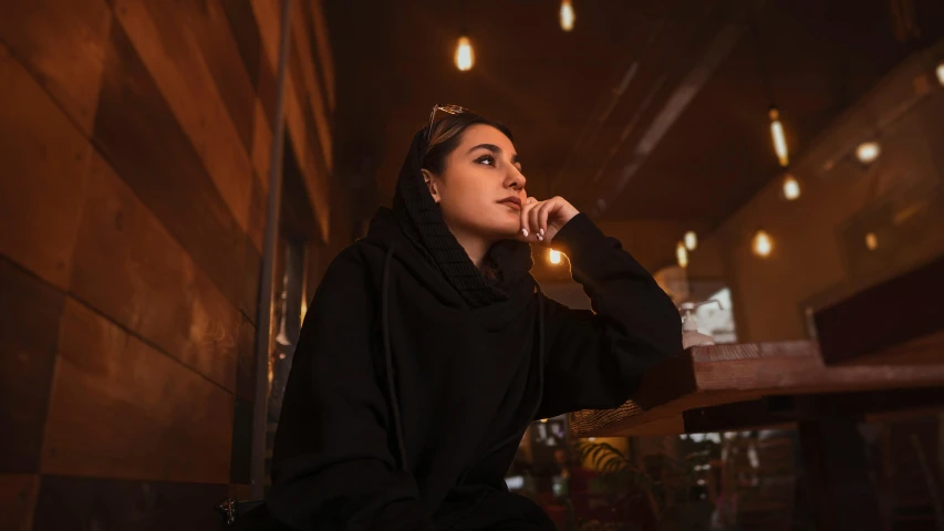 a woman sitting at a table talking on a cell phone, by Julia Pishtar, pexels contest winner, realism, dressed black hoodie, middle eastern skin, thinking pose, (night)