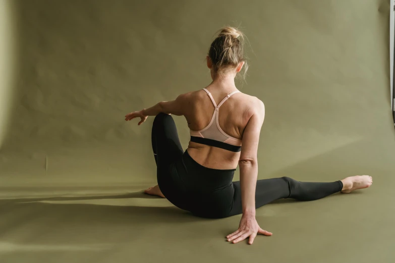 a woman sitting on the ground in a yoga pose, trending on pexels, arabesque, showing her shoulder from back, black spandex, ochre, half body cropping