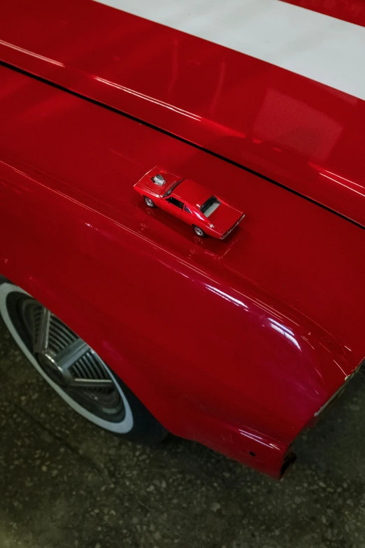 a red and white car parked in a garage, looking down on the camera, replica model, neck zoomed in, red paint detail