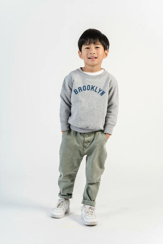 a young boy standing in front of a white background, inspired by Peter Rockwell, trending on unsplash, wearing sweatshirt, brooklyn background, wearing pants, official store photo