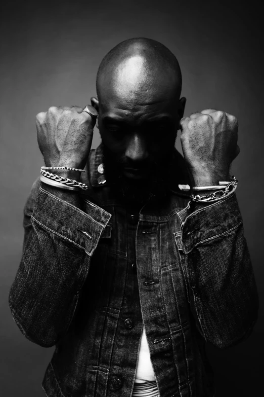 a black and white photo of a man with his hands on his head, an album cover, inspired by Terrell James, neck chains, double denim, bald male swashbuckler, dark. no text