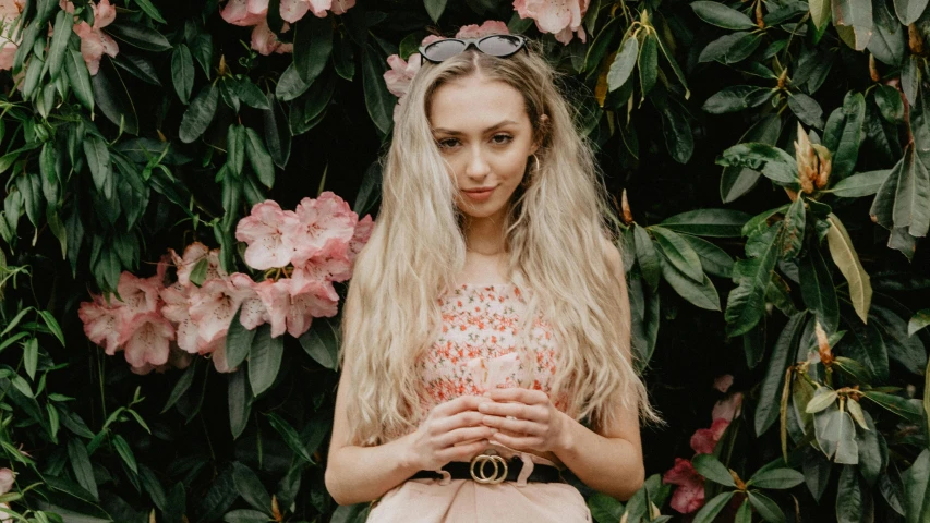 a woman standing in front of a bush of flowers, by Emma Andijewska, trending on pexels, ava max, sydney sweeney, long ashy hair, pink