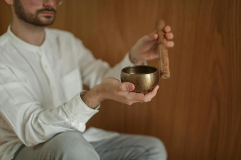 a man in a white shirt holding a metal bowl, inspired by Kanō Tanshin, trending on unsplash, holding a golden bell, yoga meditation pose, 3 / 4 wide shot, brown