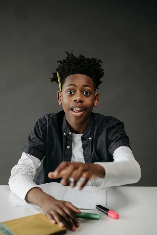 a young man sitting at a table with a notebook in front of him, inspired by Xanthus Russell Smith, pexels contest winner, hyperrealism, shrugging arms, black teenage boy, wide eyed, plain background