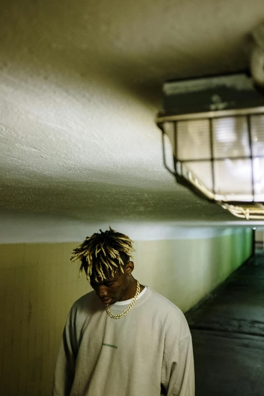 a man with dreadlocks standing in a parking garage, an album cover, unsplash, gold hair, lil uzi vert, window light, low quality photo