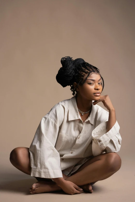 a woman sitting on the ground in a white shirt, by Chinwe Chukwuogo-Roy, trending on pexels, portrait of zendaya, plain background, box braids, muted brown