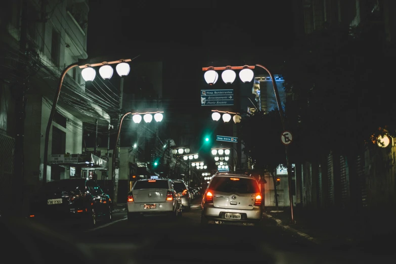 a city street filled with lots of traffic at night, a photo, unsplash contest winner, mingei, gas lamps, okinawa japan, moody aesthetic, cars parked underneath