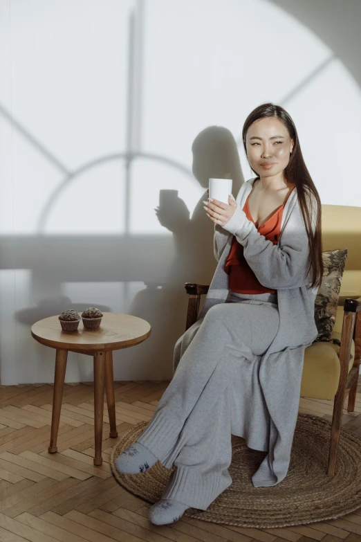 a woman sitting in a chair holding a cup, inspired by Fei Danxu, trending on pexels, dressed with long fluent clothes, grey suit, xiaoguang sun, milk and mocha style