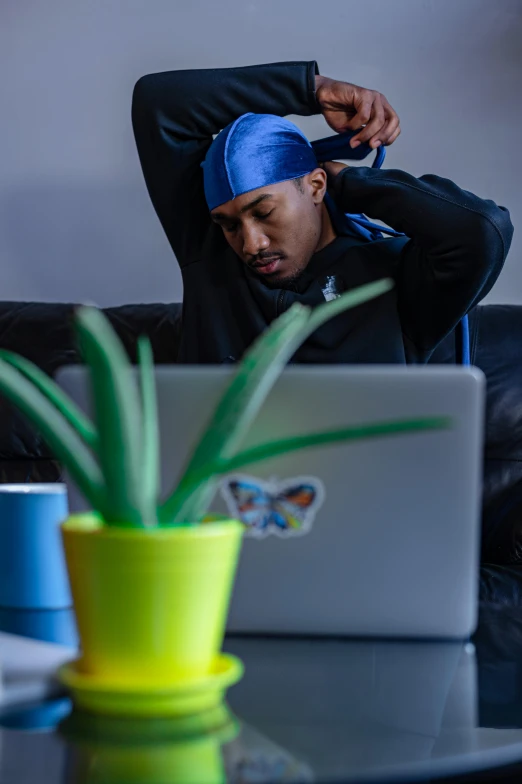 a man sitting on a couch in front of a laptop, trending on pexels, renaissance, with rap cap on head, sweating, professional sports style, bending down slightly