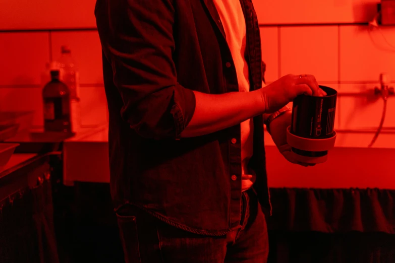 a man standing in a kitchen holding a coffee mug, by Adam Marczyński, happening, red lighting, red - black, nightclub, glowing jar