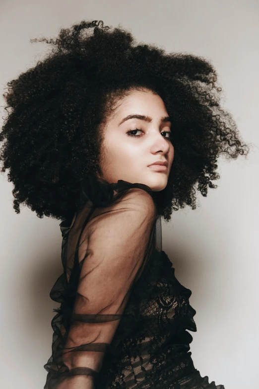 a woman with an afro is posing for a picture, shy looking down, charli bowater, deep black roots, looking towards camera