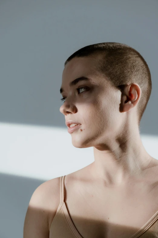 a woman with a shaved head standing in front of a wall, trending on unsplash, indoor smooth light, sophia lillis, shaven stubble, concert