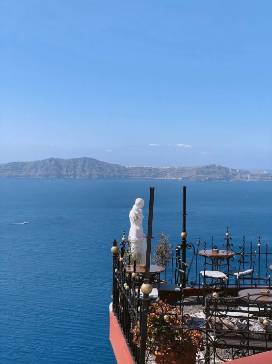 a statue sitting on top of a balcony next to the ocean, greek nose, high angel distant shot, smoldering, in the center of the image