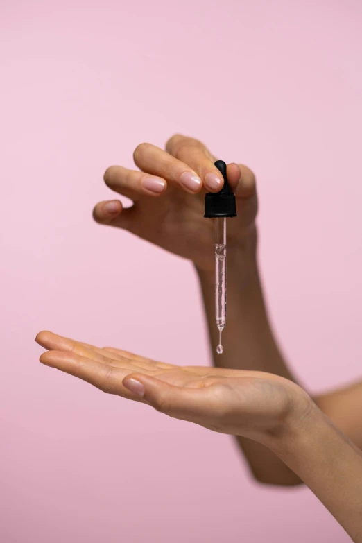 a woman holding a drop of liquid in her hand, trending on pexels, minimal pink palette, intricate oils, holding syringe, detailed product shot