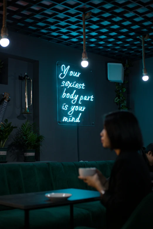 a woman sitting at a table with a cup of coffee, a hologram, trending on pexels, graffiti, neon standup bar, dark teal lighting, set on singaporean aesthetic, flirting