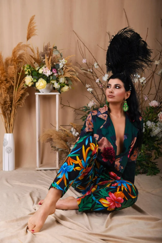 a woman sitting on a bed next to a vase of flowers, an album cover, trending on pexels, maximalism, portait of haifa wehbe, wearing a colorful men's suit, epic pose, elegant tropical prints