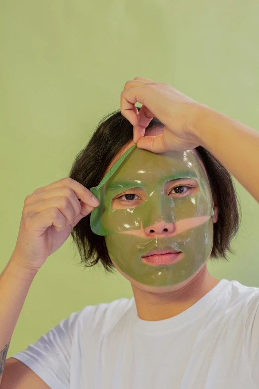 a woman putting a green mask on her face, an album cover, inspired by Ren Hang, reddit, silicone skin, clear [[bronze]] face [mask], asian male, full face