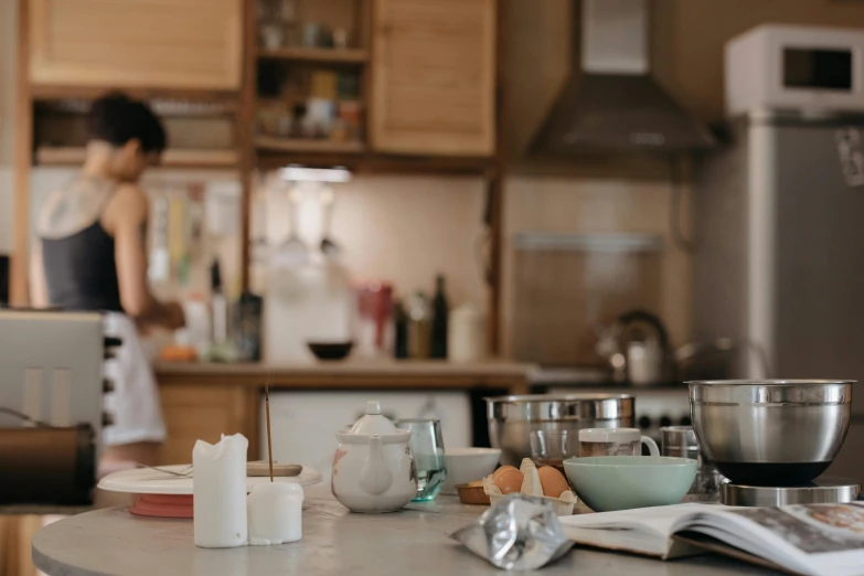 a woman standing in a kitchen next to a counter, a still life, pexels contest winner, cozy home background, silver egg cup, chefs table, family dinner