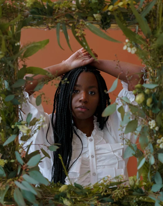 a woman standing in a bush with her hands on her head, by Dulah Marie Evans, trending on unsplash, black arts movement, botanical rainbow backdrop, sitting on a mocha-colored table, in a frame, androgynous male