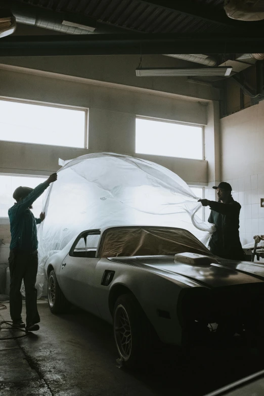 two men working on a car in a garage, pexels contest winner, conceptual art, wearing translucent sheet, restomod, wispy gigantic wings, slight overcast