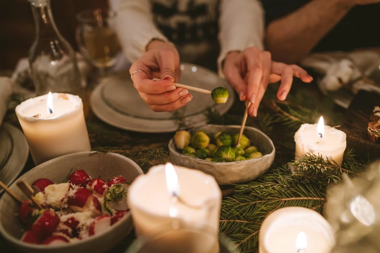 a close up of a person lighting candles on a table, by Carey Morris, pexels, vegetables on table and candle, christmas night, avatar image, people outside eating meals