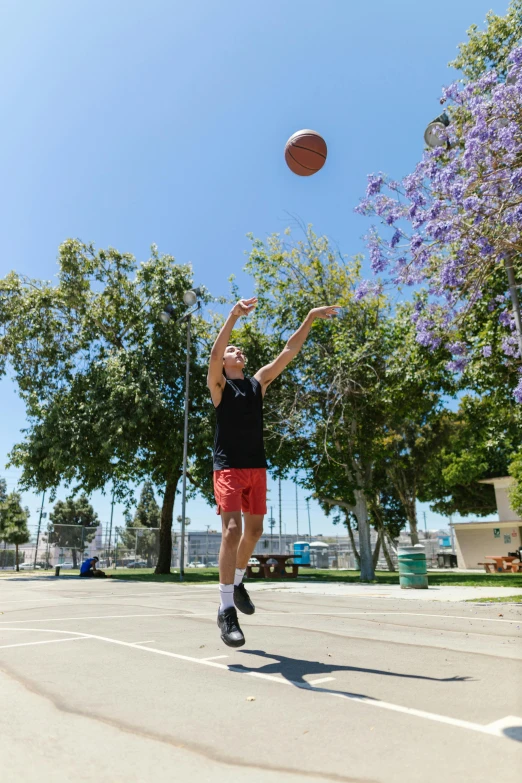 a man that is jumping in the air with a basketball, by Gavin Hamilton, dribble contest winner, happening, outside in parking lot, centered shoulders up view, wearing a tank top and shorts, asher duran