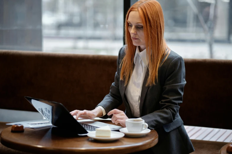 a woman sitting at a table with a laptop, pexels contest winner, private press, wearing a business suit, readhead, lachlan bailey, avatar image