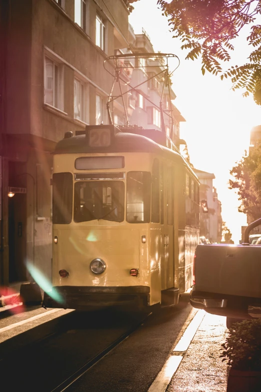 a yellow trolley traveling down a street next to tall buildings, pexels contest winner, viennese actionism, sun flares, preserved historical, hungarian, summer morning light