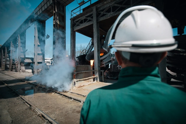 a man wearing a hard hat standing in front of a train, pexels contest winner, figuration libre, iron smelting pits, a green, worksafe. instagram photo, 4 k cinematic still