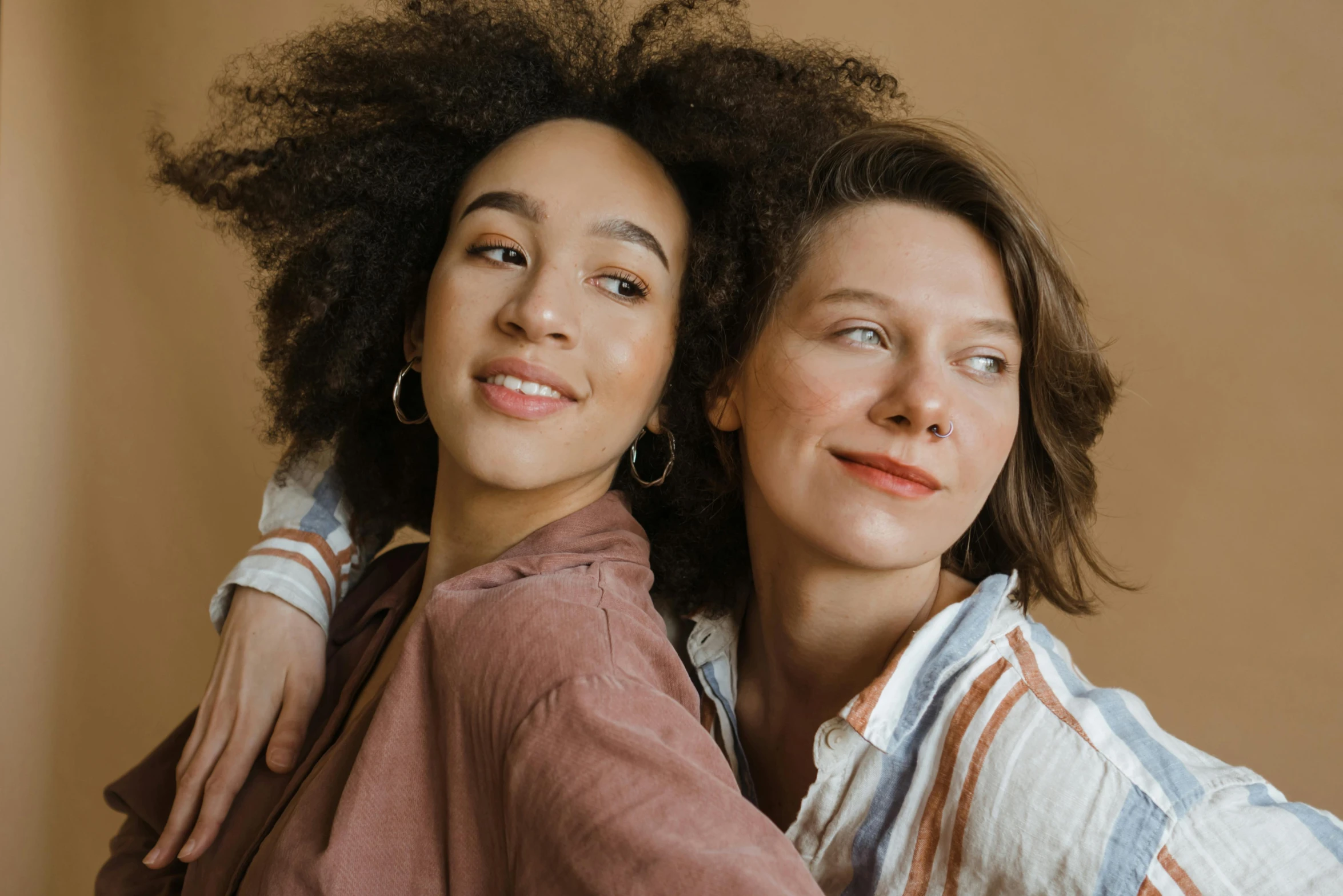 a couple of women standing next to each other, trending on pexels, brown curly hair, thumbnail, diverse, lesbian