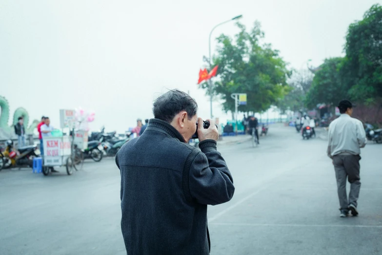 a man standing on a street talking on a cell phone, a picture, inspired by Zhang Kechun, pexels contest winner, happening, taking a picture, phuoc quan, looking across the shoulder, 4 0 years old man