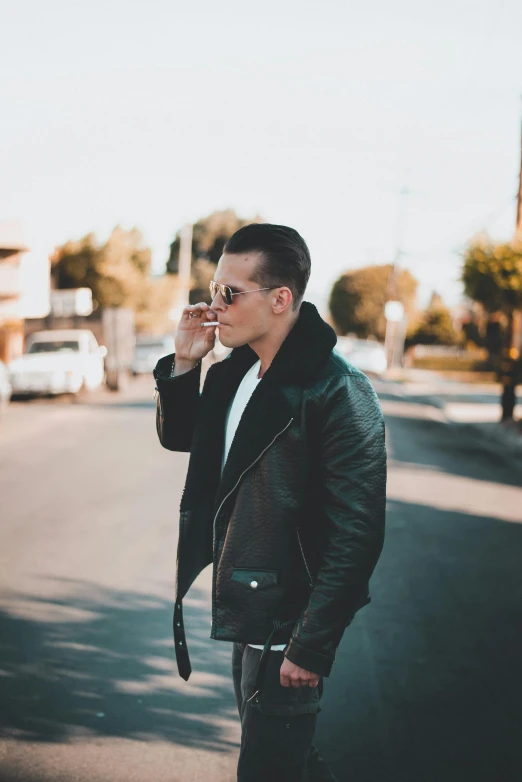 a man standing on a street talking on a cell phone, an album cover, by Robbie Trevino, trending on pexels, bauhaus, leather jacket, smoking outside, profile image, mid-shot of a hunky