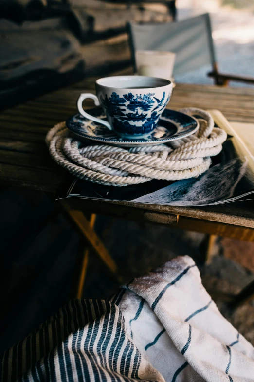 a coffee cup sitting on top of a wooden table, a portrait, inspired by Hokusai, trending on unsplash, fine art, ropes, navy, tea party, harbor
