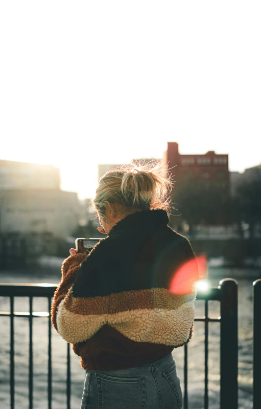 a woman standing in front of a body of water, by Niko Henrichon, pexels, winter sun, sits on a rooftop, girl with messy bun hairstyle, cell phone photo